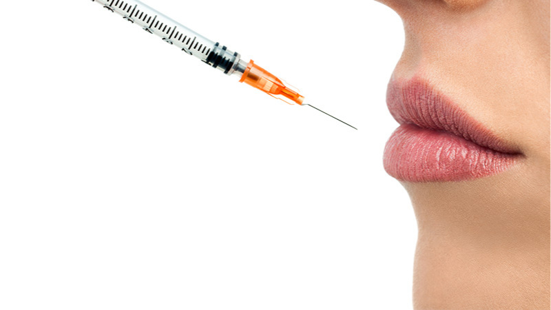 Lippen einer jungen Frau, auf die eine Spritze gerichtet ist